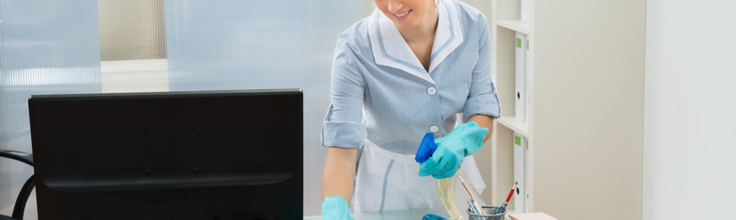 Young Female Maid Cleaning Glass Desk With Feather Duster In Office